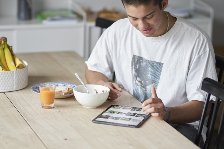 Ung mann surfer på nettbutikk ved frokostbordet