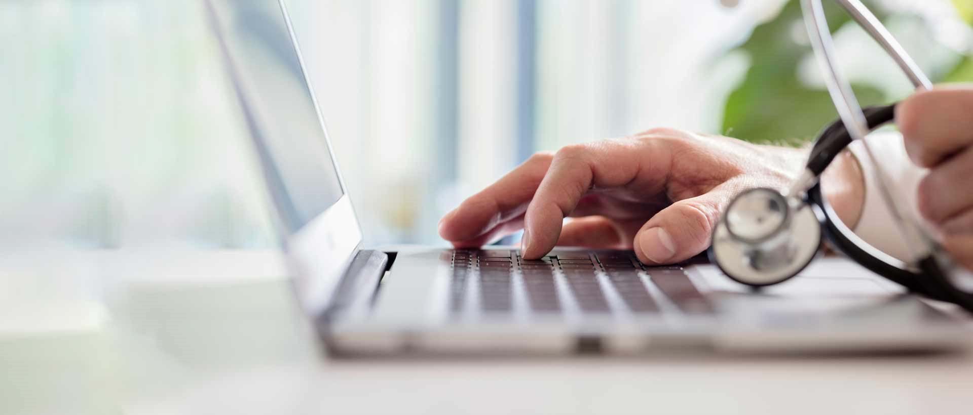 En person som jobber på sin laptop i et journalsystem. Hånden trykker på tastaturknappene..
