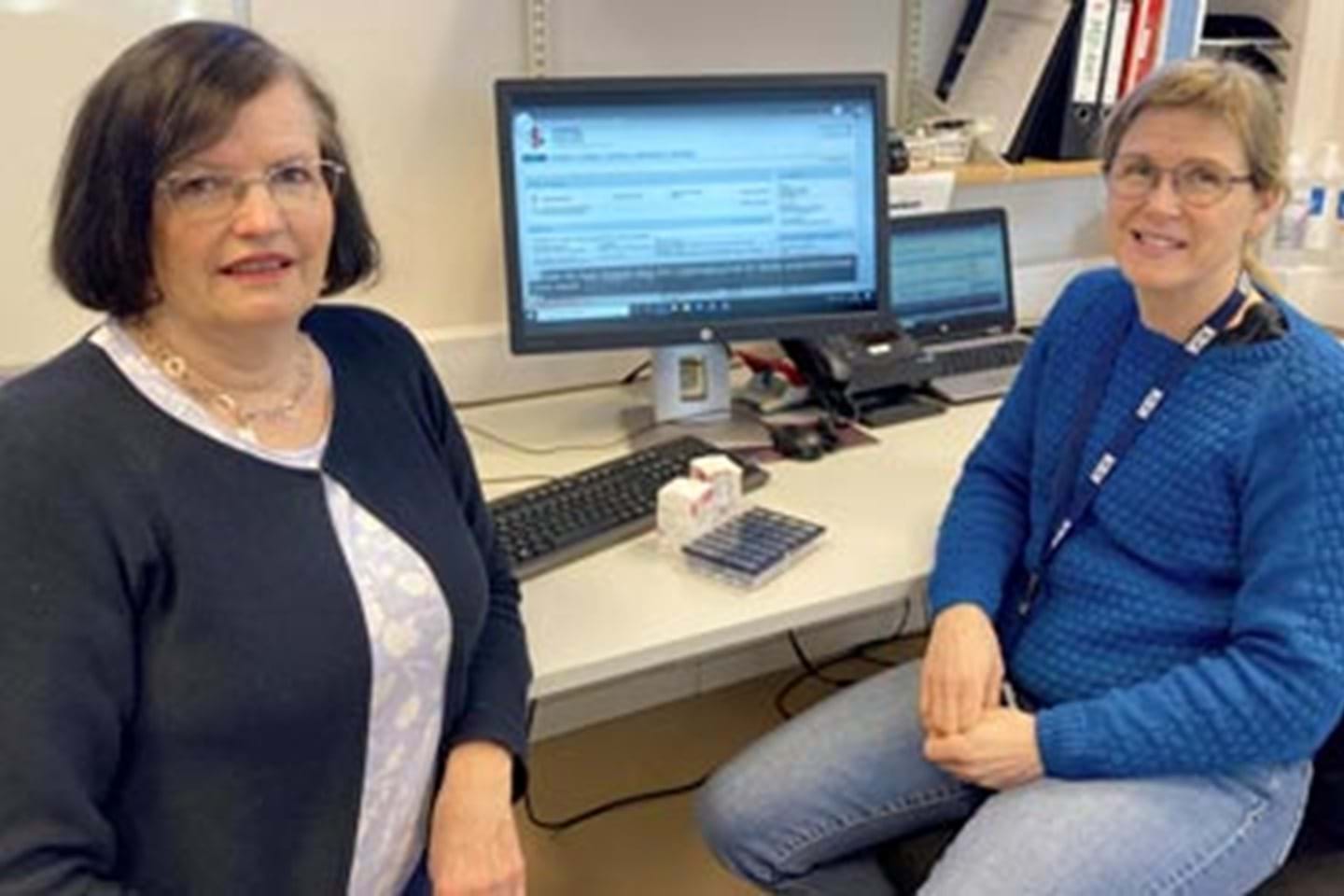 To fornøyde ansatte i Kristiansand kommune sitter ved PCen sin som er logget inn på kjernejournalen.
