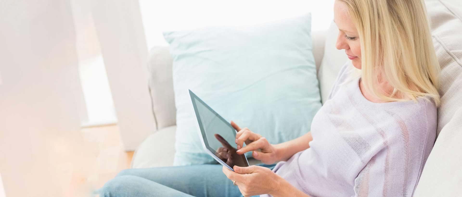 En dame som sitter hjemme i sofaen sin og har nettbrettet sitt foran seg. Digisos gir sosialtjenestens brukere mulighet til å søke sosialhjelp elektronisk.