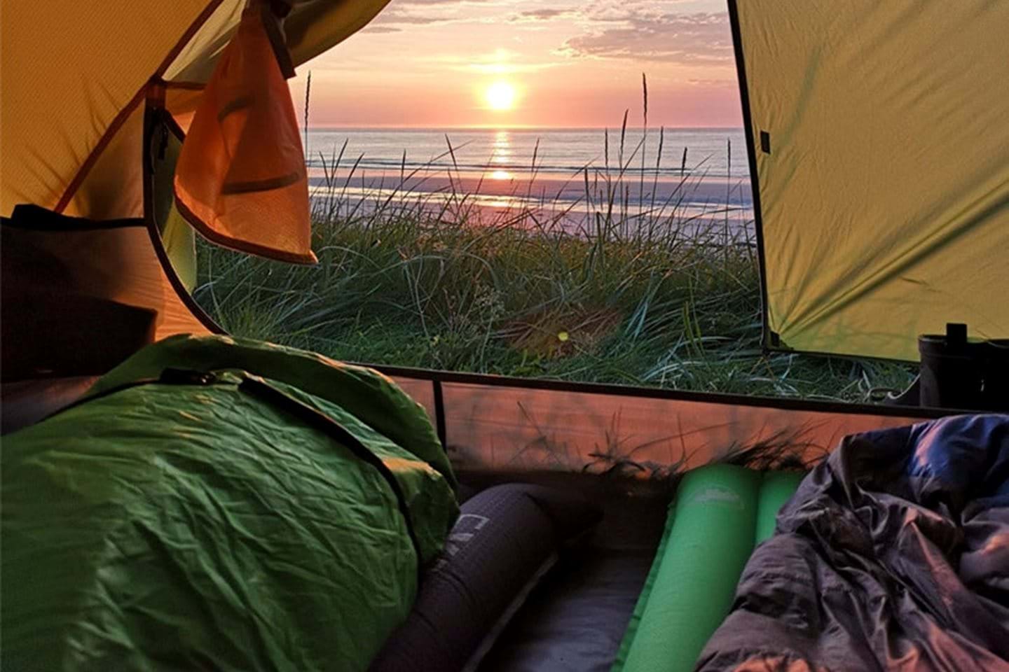 Utsikt ut fra telt til solnedgang over sjøen