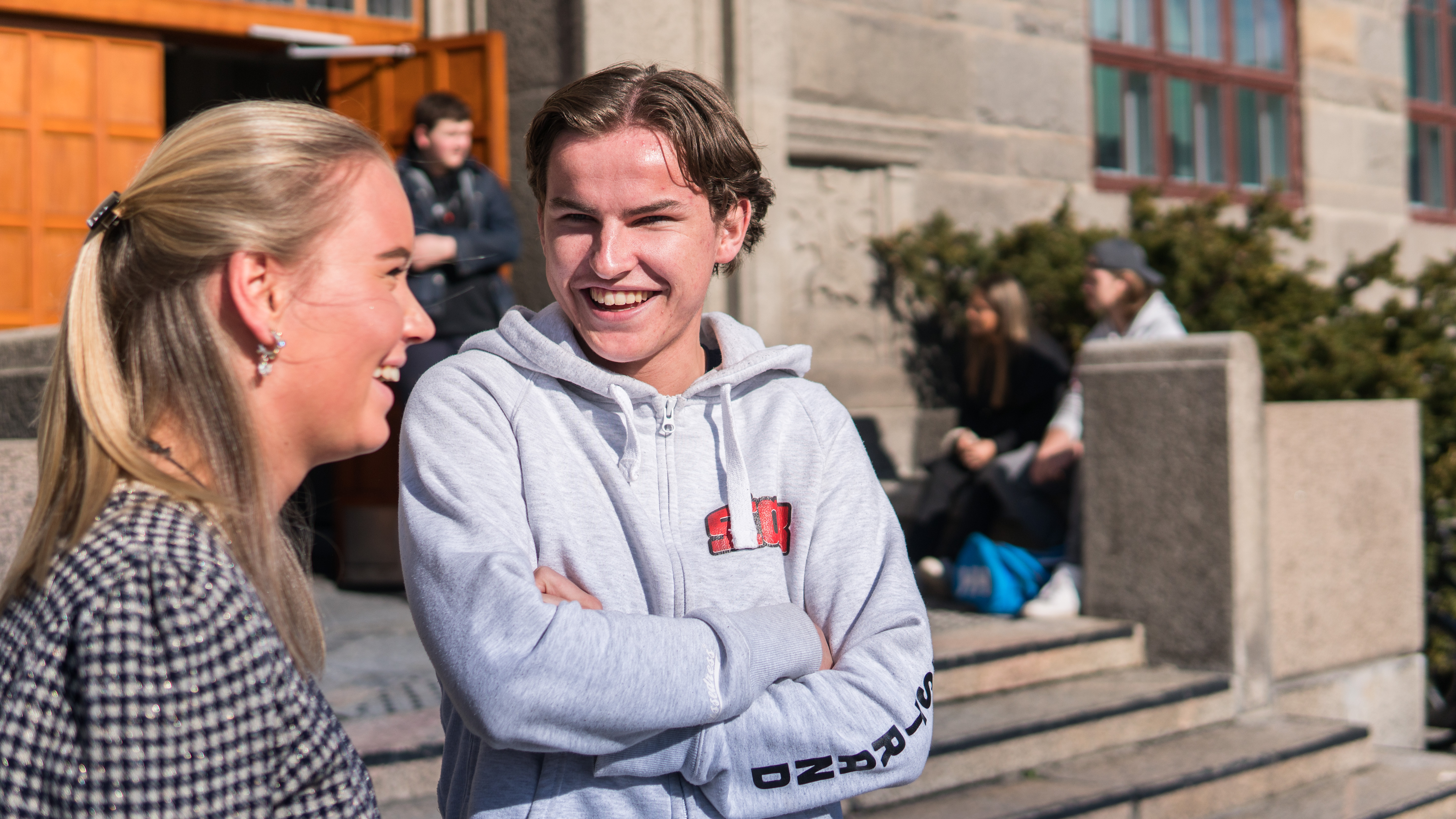 Elever som smiler og ler i samtale utenfor en videregående skole i Oslo