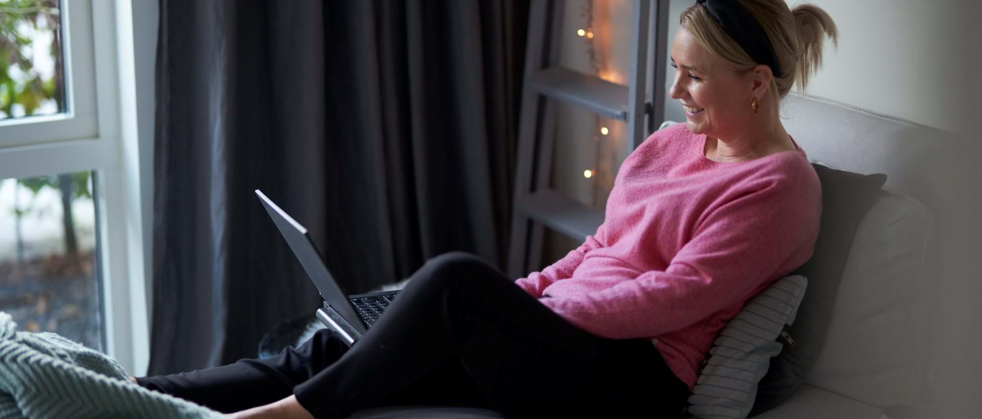 Kvinne i rosa genser ser på webinar på en laptop